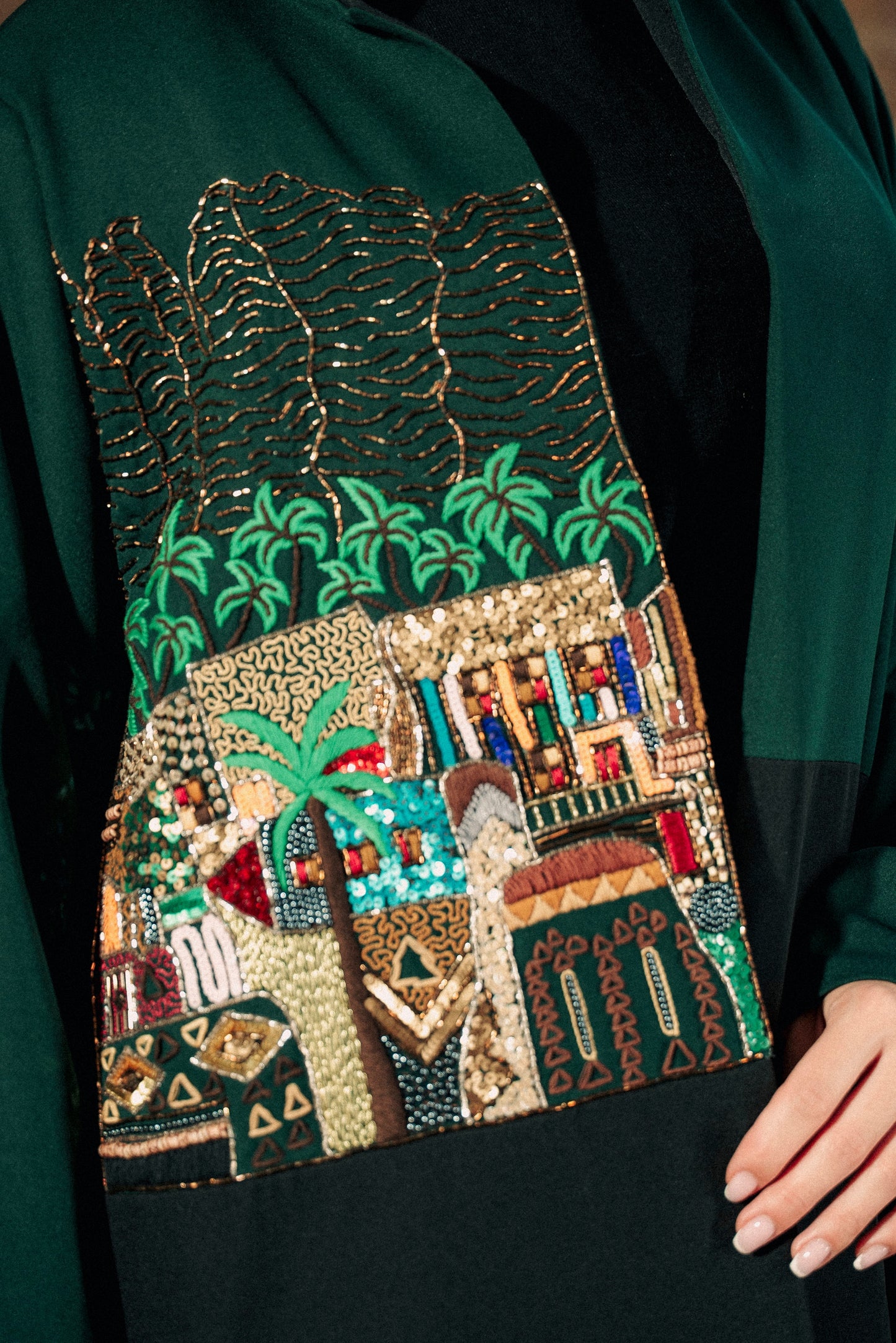 Embroidered garment with a scenic design featuring palm trees and buildings.
