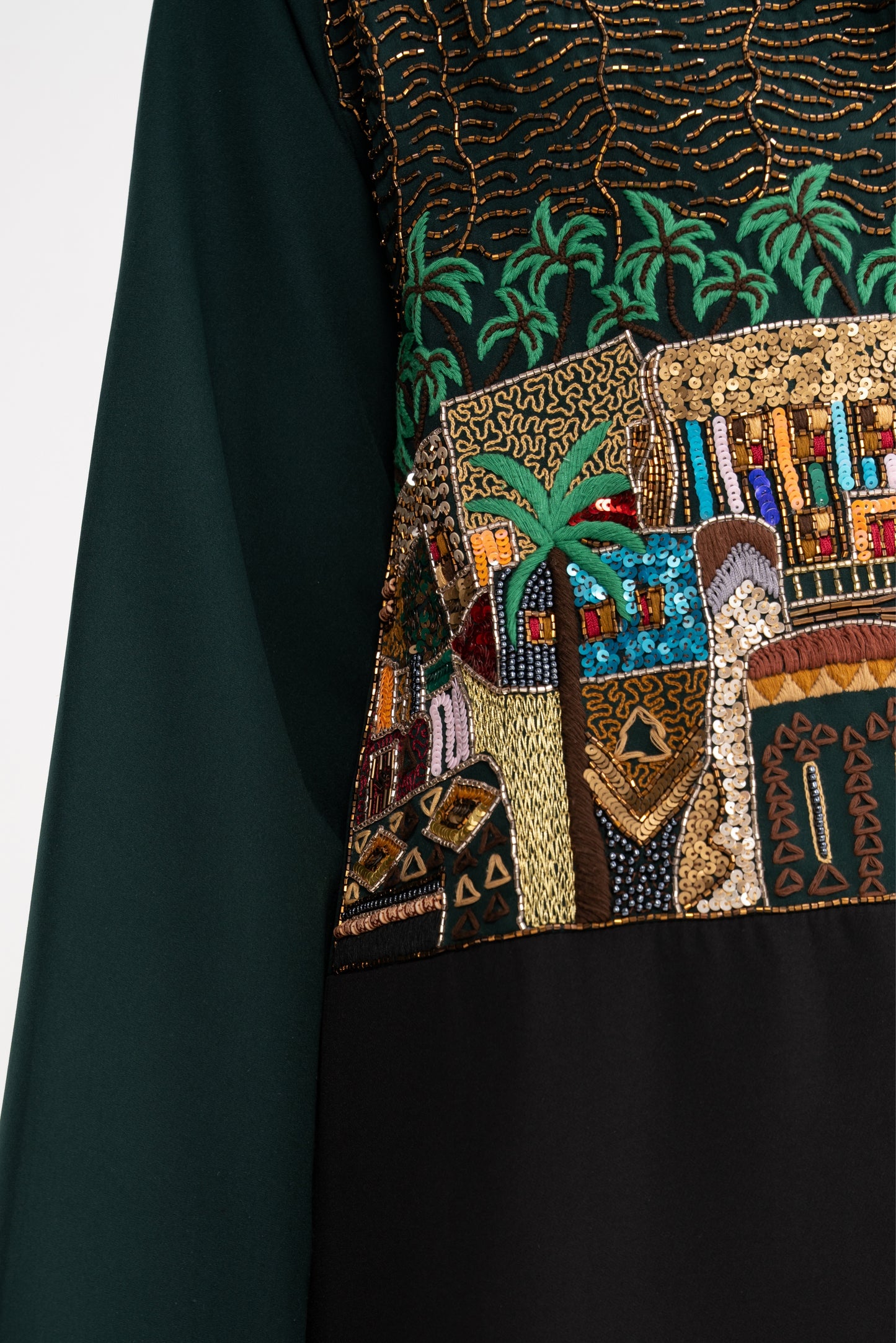 Close-up of a dark green fabric with intricate beadwork and embroidery featuring architectural elements and palm trees.